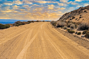 Yellow sunny clouds as dawn breaks over desert dirt road. Rocky hillside, yellow clouds and blue sky.