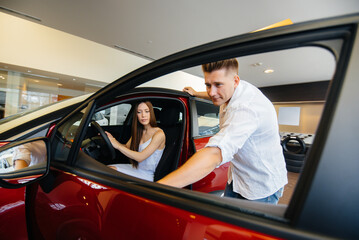 A happy young couple chooses and buys a new car at a car dealership. Buying a new car