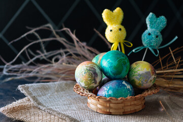 multi-colored Easter eggs of blue tones and two Easter bunny on a stick on a brown cloth background