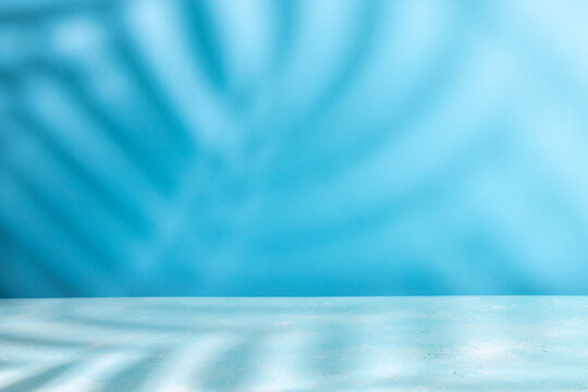 Palm coconut leaf shadow on table top and blue wall background. Abstract summer backdrop with copy space.