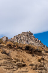 Sand and rock hillside with tall rocky peak above under a blue sky with white clouds.