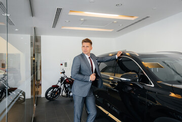 A young businessman looks at a new car in a car dealership. Buying a car