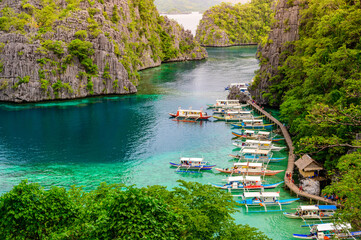 Blue crystal water in paradise Bay with boats on the wooden pier at Kayangan Lake in Coron island, Palawan, Philippines. - 427075515