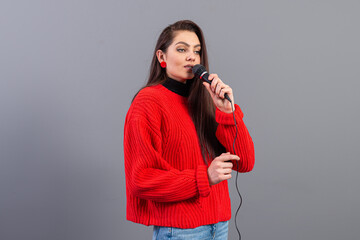 Obraz premium young, emotional brunette with a microphone dressed in a red sweater sings karaoke or says a speech