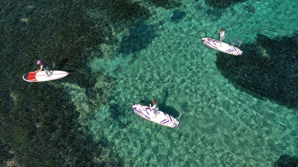 Aerial drone photo of fit women practice Stand Up Paddle or SUP in tropical exotic island shallow water emerald bay