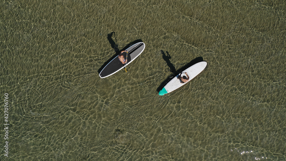 Wall mural aerial drone view of 2 men exercising sup board in emerald exotic shallow lake