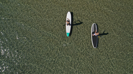 Aerial drone view of 2 men exercising sup board in emerald exotic shallow lake