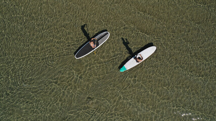 Aerial drone view of 2 men exercising sup board in emerald exotic shallow lake