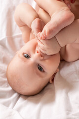 Cute baby in diapers lies in bed with white cotton linen, view from above, space for text