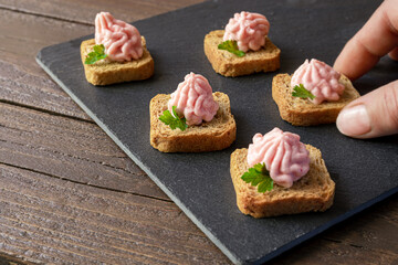 Hand takes crostini or canapes with taramasalata from a slate board