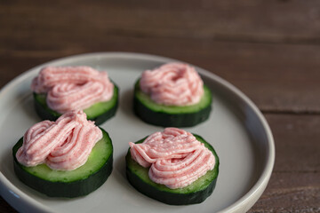 Small snacks of tarama with cucumber on a gray plate on a dark wooden table, close-up
