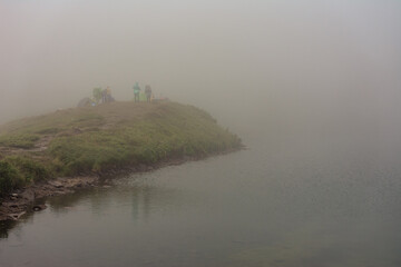 Mountain lake, tourists near a mountain lake, rain in the mountains, tourists in raincoats, fog near the lake in the Carpathians, the highest lake in the Carpathians of Ukraine Brebeneskul.