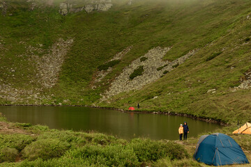 Two boys are standing by the water, two brothers are looking at the lake, the reflection in the water, the alpine lake Brebeneskul.