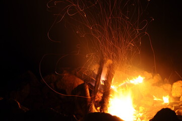 travel photography, fire in a bonfire with sparks on a long exposure side view on dark night background closeup. Selective focus
