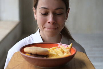 Young woman tempted by junk fast food and takes fries from plate. Selective focus, close up