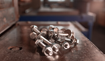 Obraz na płótnie Canvas Close-up metal chrome bolts and nuts in a chaotic order lie on the shiny metal surface of the machine. Repair and spare parts concept