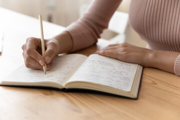 Close up view of millennial woman sit at table hold pencil take notes to paper notebook working studying. Female student businesswoman employee write records to daily planner by hand at home work desk - obrazy, fototapety, plakaty