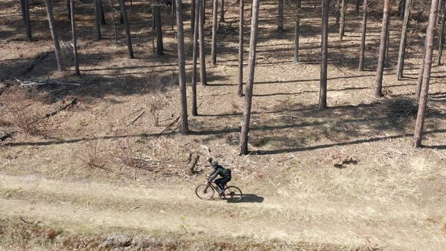 Aerial view of professional cyclist in helmet and sport clothing riding on gravel bike on a bumpy dirt road in the forest. Active lifestyle concept.