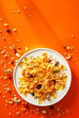 Breakfast cereal. Cornflakes, nuts, seeds and berries in a bowl with milk on orange background. Morning.