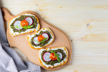 Vegan sandwiches with avocado cream on a cutting board. Healthy sandwiches with cream cheese, avocado, radish, cherry tomatoes and arugula. Copy space