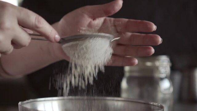 sifting flour through a small metall sieve , close up, macro, women's hands