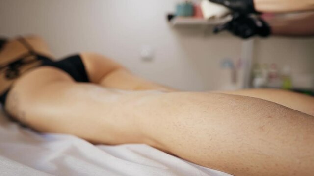 Close view on hairy leg: Female waxing or sugaring master using was device on skin