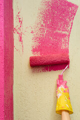 A young girl in close-up paints a yellow wall in pink. Repair of the interior.