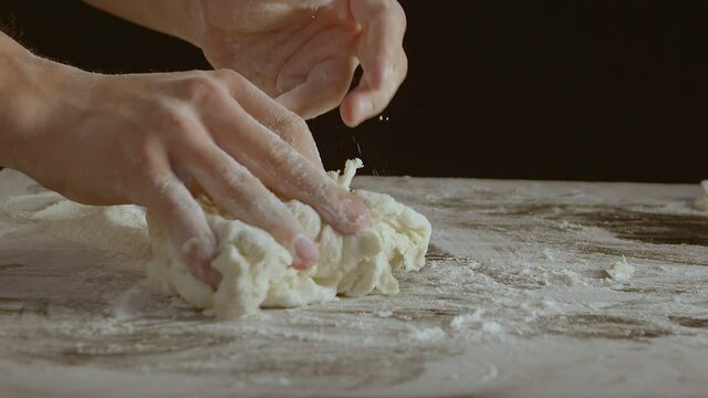 Male hands divide baking dough into three equal shares on a wooden board sprinkled with flour. Filmed on black background