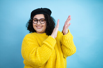 Young beautiful woman wearing french look with beret and yellow casual sweater over isolated blue...