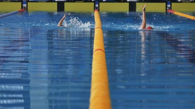 two swimmers swim on their backs along their lanes in the pool approaching the finish line. The dividing line is exactly in the middle of the frame Slow motion