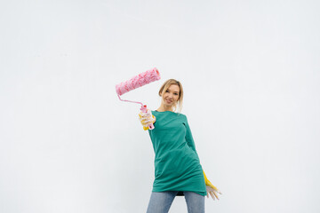 A young girl poses with a roller in front of a white wall. Repair of the interior.
