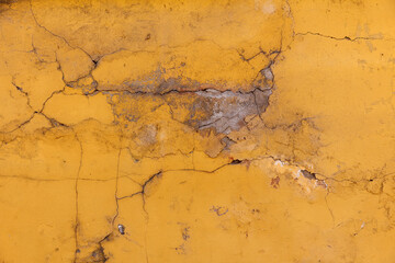 Old cracked plaster painted wall. Yellow dirty peeling plaster on a street wall as background or texture for design