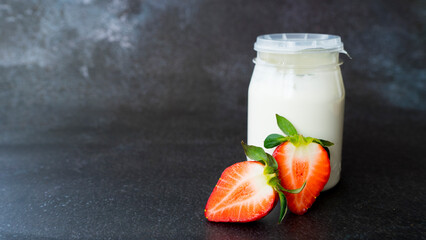 Jar with yogurt and fresh strawberries on a dark background