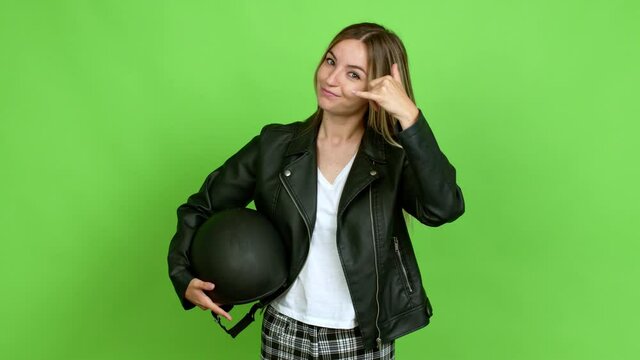 Young woman holding a motorcycle helmet making phone gesture and speaking with someone. Call me back sign over isolated background on green screen chroma key