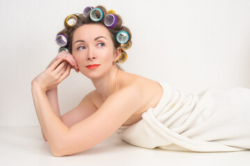 Obraz na płótnie Canvas Woman with multi-colored curlers on her head. Portrait of a woman after a shower. Girl in a towel and with curlers. Pensive girl on a white background. Concept is to create your own hairstyle