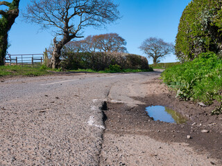 Surface damage to tarmac on a rural road is marked for repair with white spray paint. Taken on...