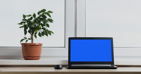 У окна стоит черный ноутбук для работы