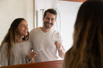Overjoyed young man and woman renters have fun brushing teeth with toothpaste together in home bathroom in the morning. Smiling millennial newlyweds couple do morning oral hygiene routine in bath.