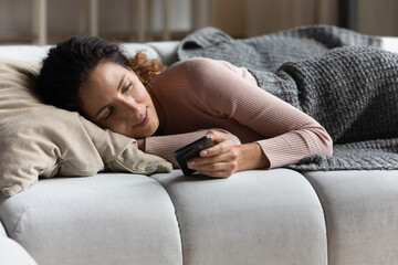 Warm words in your message. Tranquil relaxed millennial latin female lie on soft couch covered with wooden blanket read email on smartphone screen. Calm young lady browsing news on cell before bedtime