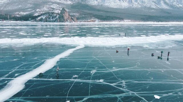 Moving drone shot following group of travellers skating on frozen lake surface. Tourists moving exploring beauty of nature with magnifficent background of mountain range and smooth ice with beautiful