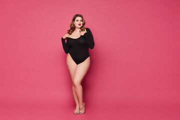 Fototapeta na wymiar Beautiful plump woman with full red lips wearing a black bodysuit against the pink background, studio shot with copy space