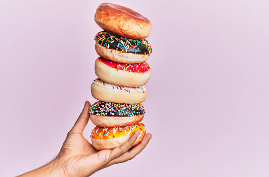 Hand of hispanic man holding tower of donuts over isolated pink background.