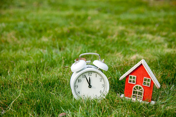White classic alarm clock with bells and toy house on green grass in a spring