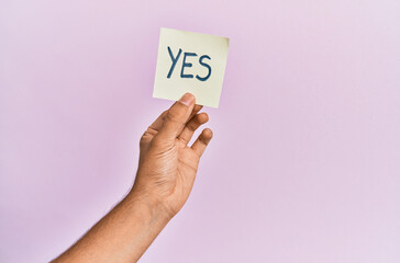 Hand of hispanic man holding yes reminder paper over isolated pink background.