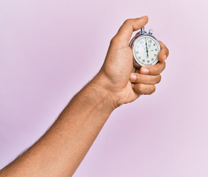 Hand of young hispanic man using stopwatch over isolated pink background.