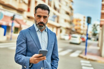 Middle age businessman with serious expression using smartphone at the city.