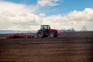 Obraz premium Modern red tractor with a plow working in a field
