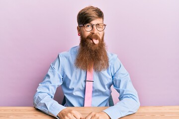 Young irish redhead man wearing business shirt and tie sitting on the table winking looking at the...