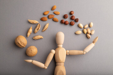 Wooden mannequin juggling nuts on gray pastel background. close up.