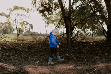 Cute little caucasian boy walking in nature wearing blue gumboots